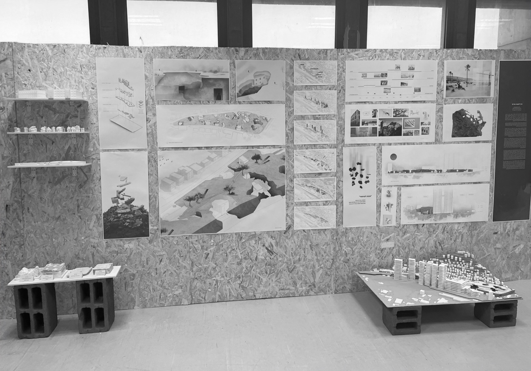Final review presentation boards pinned to an OSB wall, with physical site and concept models displayed on cinder blocks